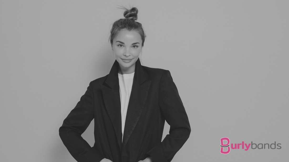 A lady wearing a black jacket and white top with her hair tied in a high bun