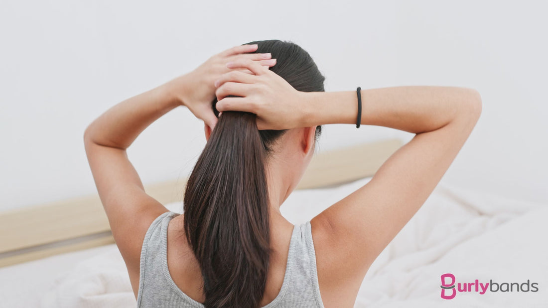 A lady with a hair tie on her wrist tying hair into a pony