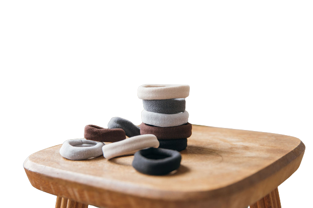 Burlybands sitting on a stool stacked up. Black hair ties, grey hair ties, white hair ties all one on top of the other
