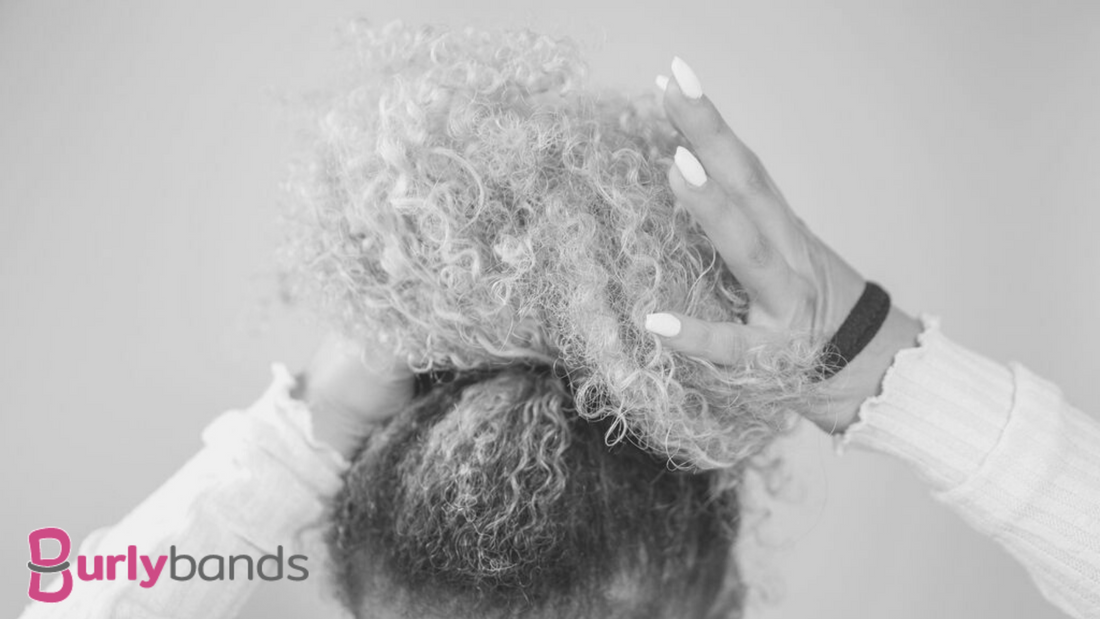 A lady with very curly hair holding it up in top of her head to put a band on